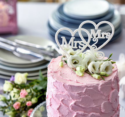 A pink wedding cake with Mrs. and Mrs. on the top. 