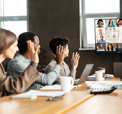 People raising hands looking at computer with conference meeting on screen
